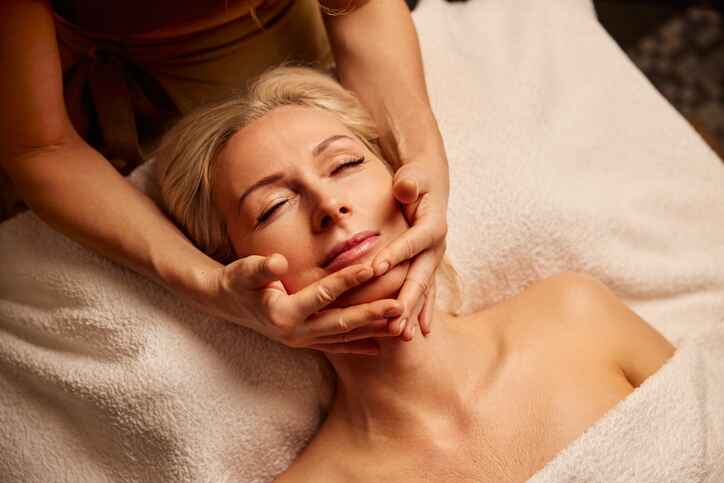Massage therapy Lansing MI relaxation treatment with hands along jawline in calming setting.